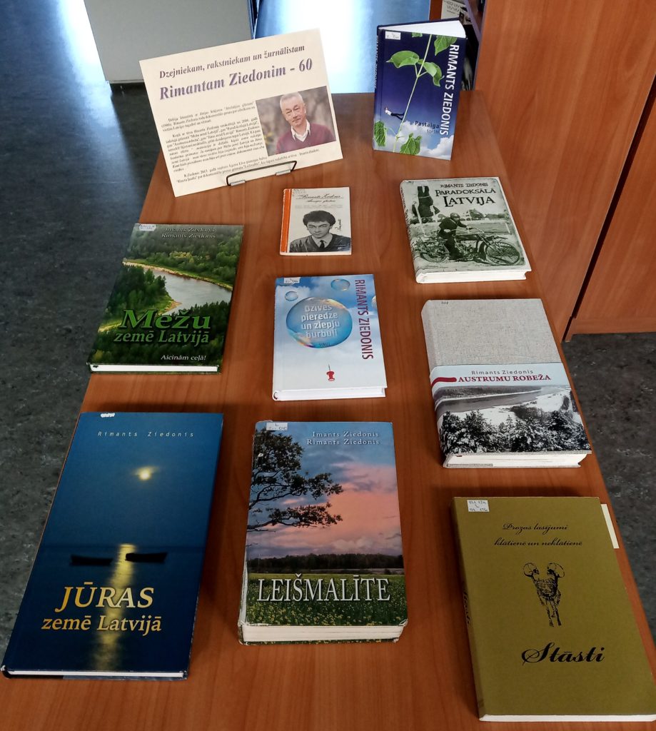 galds, uz kura izkārtotas vairākas grāmatas un lapa. Uz lapas piemin Rimantu Ziedoni un norāda, ka viņam ir 60 gadi. Grāmatu vidū ir darbi, kas saistīti ar Latviju un tās dabu, piemēram, "Mežu zeme Latvijā," "Jūras zeme Latvijā," "Leismalite" un citas.