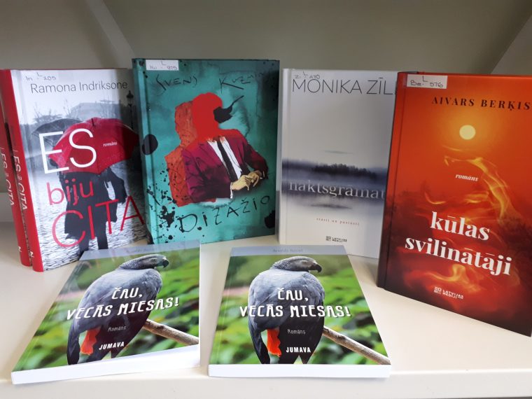 Stāvos saliktās četras dažādas grāmatas, divas grāmatas guļus