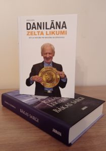 grāmata ar nosaukumu “DANILĀNA ZELTA LIKUMI”. Priekšplānā ir cilvēks, kurš tur lielu zelta medaļu. Fons ir koka virsma un neitrālas krāsas siena. Apakša grāmata "Bākas sargi"