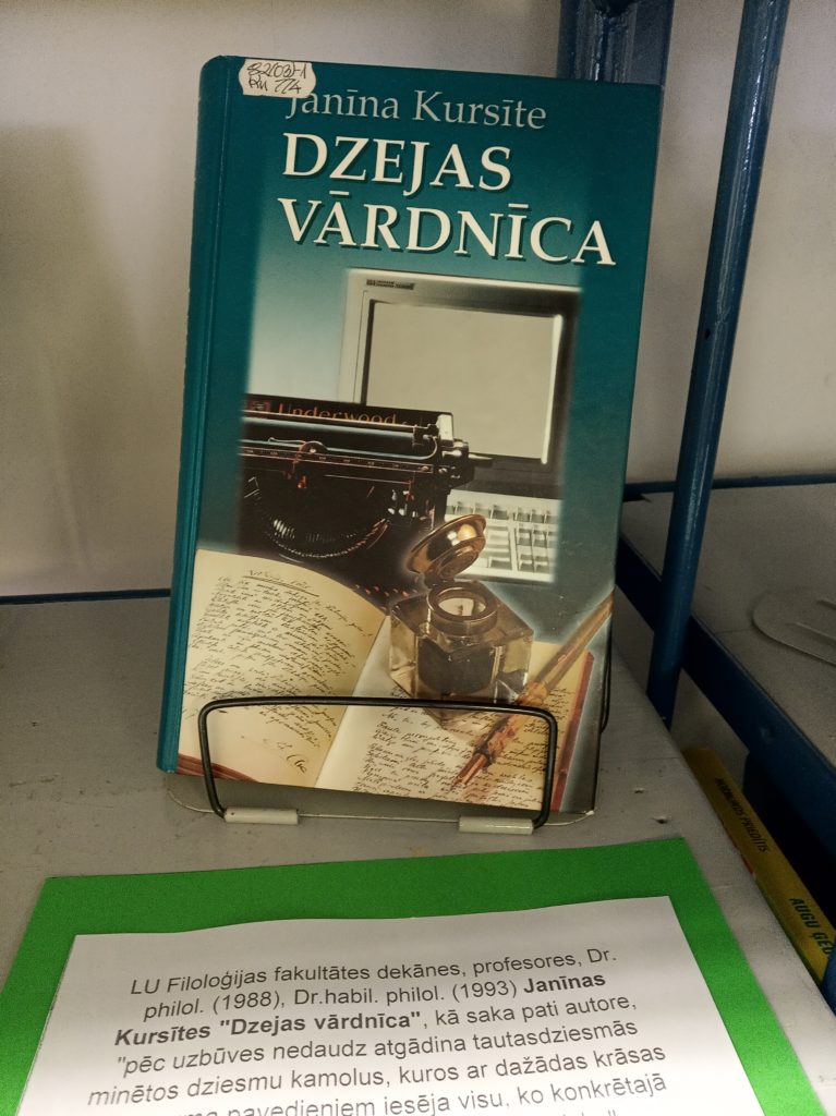 redzama grāmata ar nosaukumu “Dzejas vārdnīca” autors Janīna Kursīte. Uz vāka ir attēlots vecmodīga rakstāmmašīna un vairākas papīra lapas,. Zem grāmatas ir teksts latviešu valodā, kas, iespējams, ir biogrāfiska informācija par autoru vai saistīta ar grāmatas izdošanu.