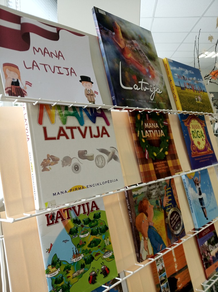 No sānskata redzami izlikti uz statīvā vairākas grāmatas bērniem. Uzraksts " Mana Latvija"
