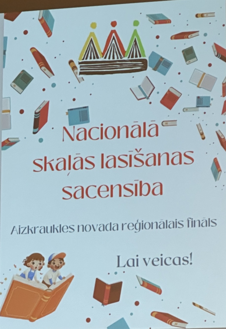 Krāsains plakāts. Augšpusē ir krāsains kronis, zem kura ir teksts latviešu valodā “Nacionālā skaļas lasīšanas sacensības,” un mazāks teksts “Aizkraukles novada fināls.” Ir arī ilustrācijas ar diviem bērniem, kuri ir uz atvērtās grāmatas, lido starp citām grāmatām un zīmuļiem. Apakšā ir uzraksts “Lai veicas!